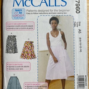 May include: McCall's sewing pattern M7960, designed for beginners. The pattern includes instructions for patch pockets, tie ends, and gathers. The image shows a woman wearing a white dress. The pattern size is A5 (6-8-10-12-14).