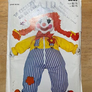 May include: A vintage sewing pattern for a clown doll. The pattern is from Butterick and is number 3510. The doll is wearing a yellow shirt, blue and white striped overalls, and red shoes. The pattern is for one size.