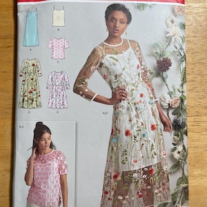May include: Simplicity sewing pattern 8545 D5. The pattern features a woman wearing a white dress with floral embroidery. The pattern also shows other dress and top designs. The size is US 4-12.