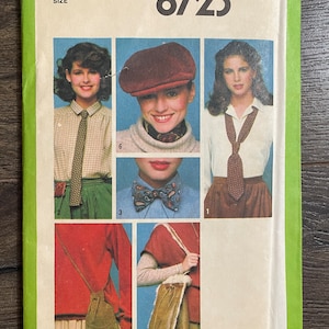 May include: Simplicity sewing pattern number 8723 for a one-size outfit. The pattern includes a shirt with a bow tie, a shirt with a tie, a hat, a bag, and a skirt. The pattern is on a green background with the text "Simplicity" and "$1.75" in white.