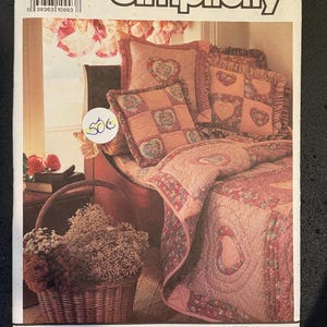 May include: Simplicity sewing pattern number 7138 for a quilt and pillows with a heart design. The pattern is by Shirley Botsford and includes instructions for making a quilt and pillows with a heart design. The quilt and pillows are pink and white with a floral print.