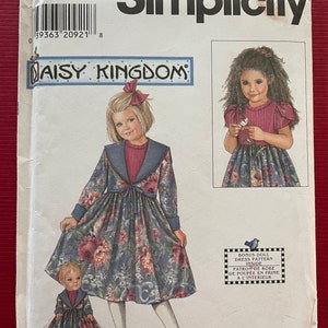 May include: Simplicity sewing pattern number 7867 for a Daisy Kingdom dress. The pattern includes a bonus doll dress pattern. The pattern cover features two girls wearing dresses with floral prints. The text "Daisy Kingdom" is printed in a banner at the top of the pattern cover.