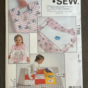 May include: A Kwik Sew pattern 1798 for baby items. The pattern includes instructions for a tote bag, bib, blanket, and play mat. The items feature a pink and white striped fabric with cartoon animal designs. The pattern is designed by Kerstin Martensson.