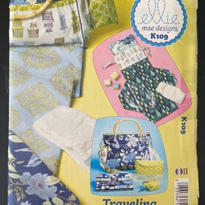 May include: A sewing pattern envelope for Ellie Mae Designs K109 Traveling Totes For Tots. The yellow package displays various fabric bags, a changing pad, and accessories featuring blue, green, and white floral, bird, and raindrop patterns.