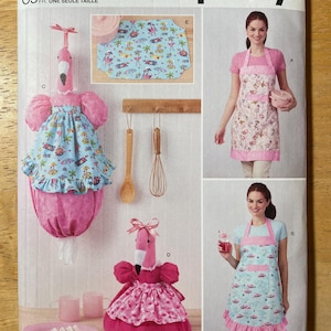 May include: Simplicity sewing pattern S9973 featuring flamingo-themed kitchen accessories and aprons. The pattern includes a flamingo-shaped paper towel holder, a pot holder, and two apron designs with coordinating fabric. The pattern is one size.