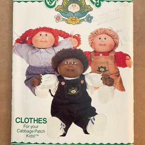 May include: A sewing pattern for Cabbage Patch Kids clothes. The pattern shows three dolls wearing different outfits: a red-haired doll in a striped shirt and denim dungarees, a brown-skinned doll in a white shirt and denim dungarees, and a blonde doll in a red shirt and denim dungarees. The pattern is from Butterick and has the number 6508.