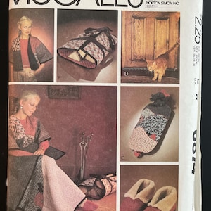 May include: A McCall's sewing pattern envelope featuring illustrations of quilted garments and accessories including a jacket, a wrap, a hot water bottle cover, and slippers with faux fur lining, all displayed with various fabric patterns.
