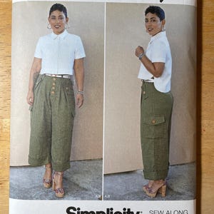 May include: A Simplicity sewing pattern featuring a woman wearing a white collared shirt and olive green cargo pants. The pattern includes the text "Mimi G Style" and "Simplicity" with size information.