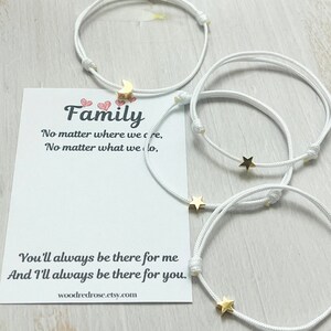 Op de afbeelding: Vier witte koordarmbanden met kleine goudkleurige bedels in de vorm van een halve maan en sterren. Een witte presentatiekaart is inbegrepen met de tekst: Family, No matter where we are, No matter what we do, You'll always be there for me And I'll always be there for you.