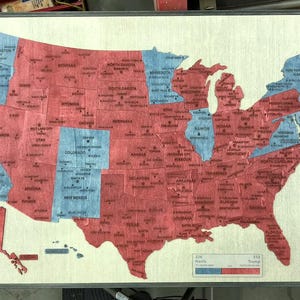 May include: A framed map of the United States, with states coloured in red and blue. The map shows the states and their names. A small chart at the bottom indicates the number of votes for each colour.