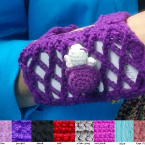 May include: Purple crocheted phone case with a white crocheted flower embellishment. The case has a white background with a purple grid pattern. The text "B Home" is visible on the case.