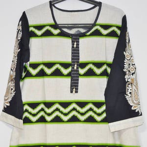 May include: A white and black striped tunic with green geometric patterns. The sleeves are black with gold embroidery.