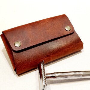 May include: A brown leather travel case with a flap closure and two metal snaps. The case is designed to hold a safety razor.