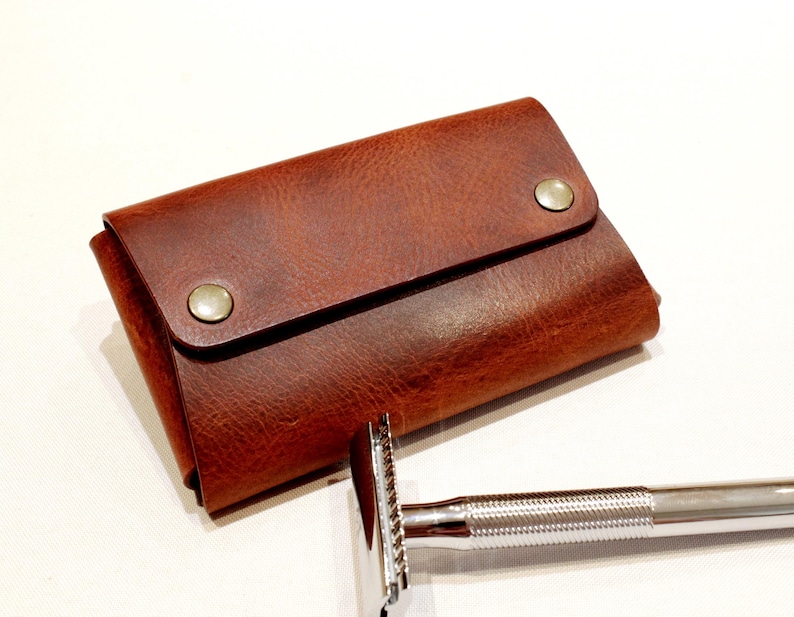 May include: A brown leather travel case with a flap closure and two metal snaps. The case is designed to hold a safety razor.