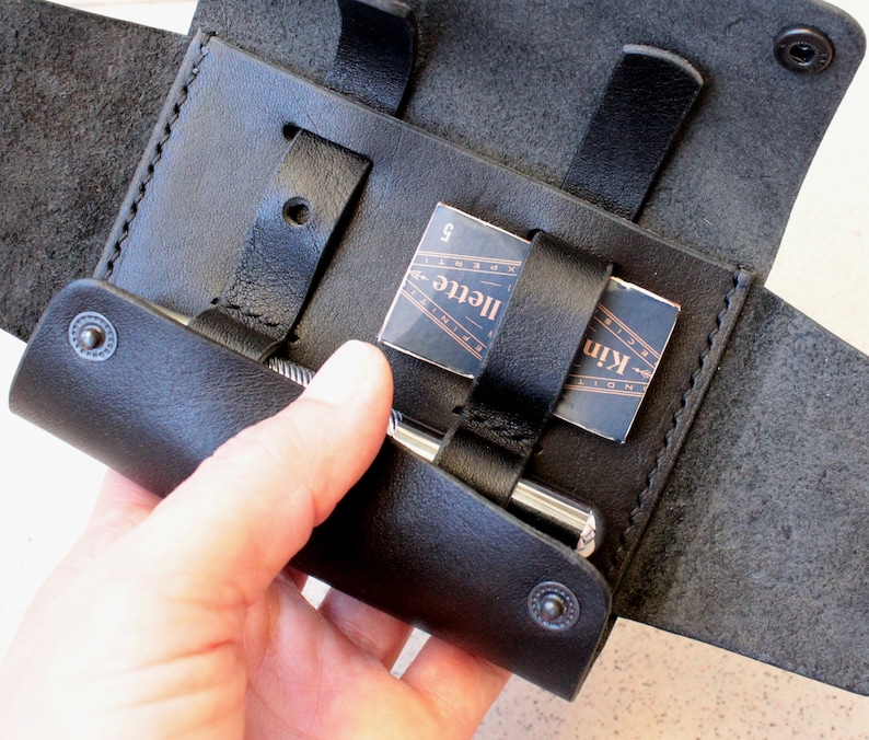 May include: A black leather case with a flap that opens to reveal a silver pen and a small card with the text "Kinfolk" and "Illete" printed on it.