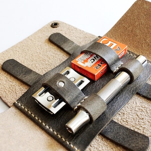 May include: A brown leather travel case with a razor, a razor blade, and a silver metal shaving brush. The case has a flap that closes with a snap.