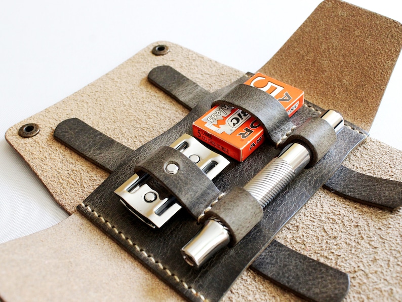 May include: A brown leather travel case with a razor, a razor blade, and a silver metal shaving brush. The case has a flap that closes with a snap.
