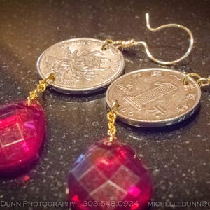 May include: A pair of earrings with red glass teardrop-shaped pendants and gold-colored chains. The earrings are attached to Chinese coins with a gold-colored wire.