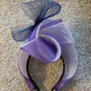 May include: A purple and white headband with a blue mesh bow. The headband is made of a soft, stretchy material and is perfect for adding a touch of elegance to any outfit.