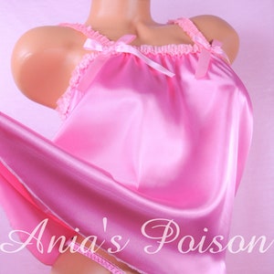 May include: Pink satin lingerie set featuring a camisole top with lace trim and bow accents, paired with matching thong underwear. The set is made of a shiny, smooth fabric. The text "Ania's Poison" is visible.