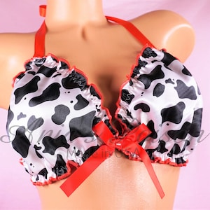 May include: A black and white cow print satin bralette with red ruffled trim and a red satin bow in the center.
