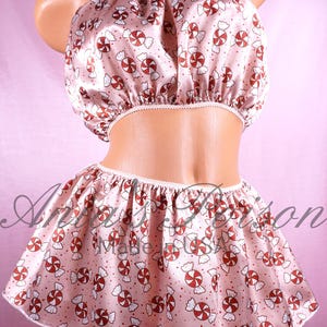 May include: A pink satin skirt and matching top with a candy cane print. The skirt is gathered at the waist and has a white trim. The top is a strapless bandeau style.
