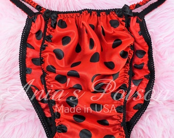 May include: Red satin underwear with black polka dots and black trim. The underwear has adjustable straps and a bow on the front. "Made in USA" is printed on the front.