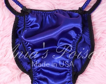 May include: Royal blue satin underwear with black lace trim and small black bows. The text "Inia's Poise" and "Made in USA" are visible on the garment. The fabric has a shiny, smooth texture.