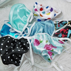 May include: Assortment of satin fabric face masks in various colors and patterns, including black and white polka dots, blue with white polka dots, light blue, floral print, and a white mask with colorful polka dots.