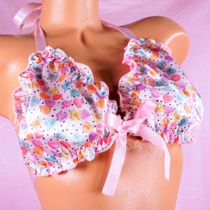 May include: Pink satin bra with ruffled edges and a pink satin bow. The bra is covered in a pattern of colorful candy hearts with the words "Be Mine", "Love You", "XOXO", and "I Love You" printed on them.