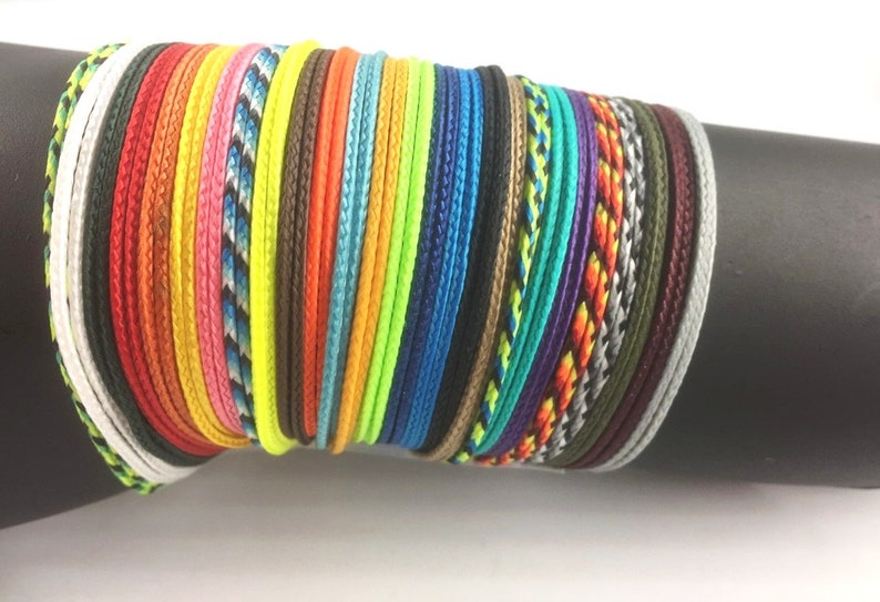 May include: A stack of colorful braided cords, including black, white, red, orange, yellow, green, blue, purple, and grey.