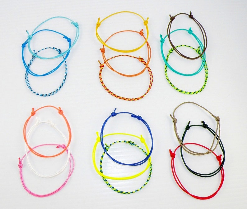 May include: A set of eight colorful friendship bracelets, each made of braided string. The bracelets are in various colors, including blue, orange, yellow, green, brown, and red.
