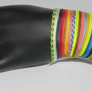 May include: A stack of colorful bracelets made of woven string. The bracelets are in various shades of blue, green, yellow, red, and orange. The bracelets are on a black mannequin hand.