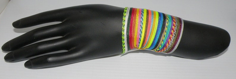 May include: A stack of colorful bracelets made of woven string. The bracelets are in various shades of blue, green, yellow, red, and orange. The bracelets are on a black mannequin hand.