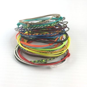 May include: A stack of colorful braided bracelets in various colors, including red, orange, yellow, green, blue, and purple.
