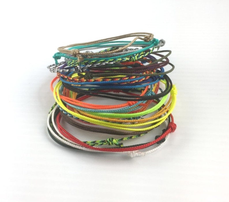 May include: A stack of colorful braided bracelets in various colors, including red, orange, yellow, green, blue, and purple.