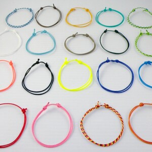 May include: Assortment of 20 colorful braided friendship bracelets. The bracelets are made of thin cord and have a simple knot design. The colors include blue, green, red, orange, yellow, pink, white, black, brown, and gray.