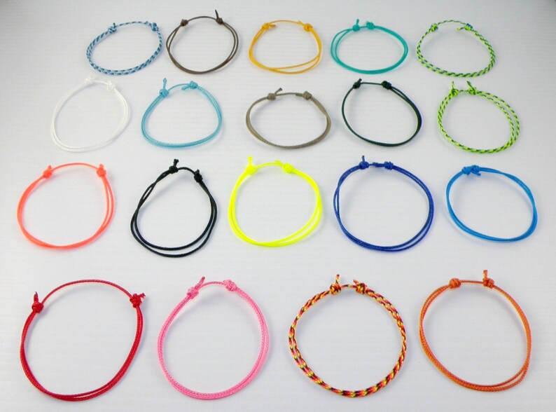 May include: Assortment of 20 colorful braided friendship bracelets. The bracelets are made of thin cord and have a simple knot design. The colors include blue, green, red, orange, yellow, pink, white, black, brown, and gray.