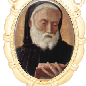 Puede incluir: Colgante dorado con un retrato ovalado de un hombre con barba blanca y túnica negra, leyendo un libro. El retrato está enmarcado por un borde ornamental y decorativo con lazos en la parte superior e inferior para una cadena.