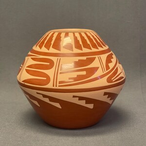 May include: A hand-painted, round pottery vessel with a light tan base and intricate rust-colored geometric designs. The vessel features a series of stepped patterns and curved lines, showcasing traditional craftsmanship. The pottery is likely used for decorative purposes.