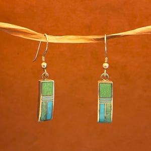 May include: A pair of silver earrings with rectangular pendants. Each pendant features a green top section, a turquoise middle section, and a turquoise bottom section. The earrings hang from silver hooks.