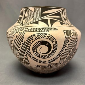 May include: A black and white hand-painted pottery jar with geometric designs. The jar has a rounded body and a wide mouth.