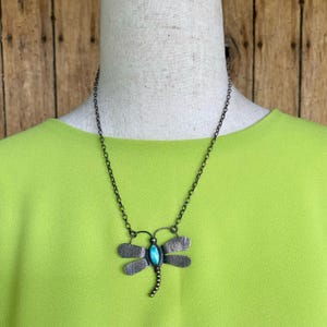May include: A silver necklace with a turquoise dragonfly pendant. The dragonfly has detailed wings and a beaded body.