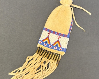 May include: A tan suede pouch with a beaded design featuring crosses and geometric patterns in red, blue, and yellow. The pouch has a drawstring closure and is adorned with hanging fringe and metal accents.