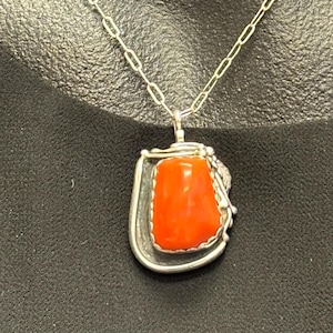 May include: A silver pendant necklace featuring a vibrant orange stone. The stone is set in a silver frame with decorative accents. The necklace has a delicate silver chain, perfect for everyday wear.