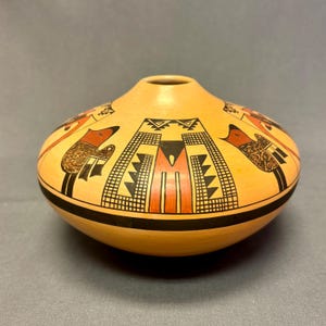 May include: A hand-painted, round pottery vessel with a narrow neck. The beige-colored pot features a black, red, and brown geometric design with bird-like figures. A thick black band encircles the base of the pot.