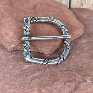 May include: A silver belt buckle with a twisted rope design.