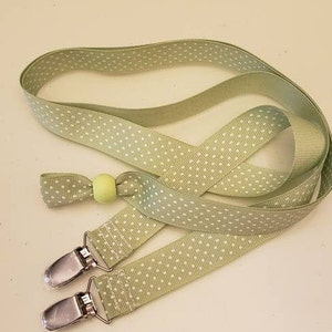 May include: A pale green pacifier clip with white polka dots. It features two metal clasps and a small, round, yellow bead. The ribbon is folded and looped.