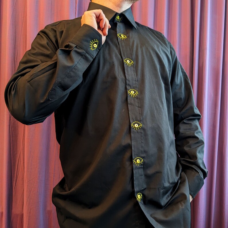 May include: A black long-sleeved button-down shirt with yellow embroidered eyes down the front.