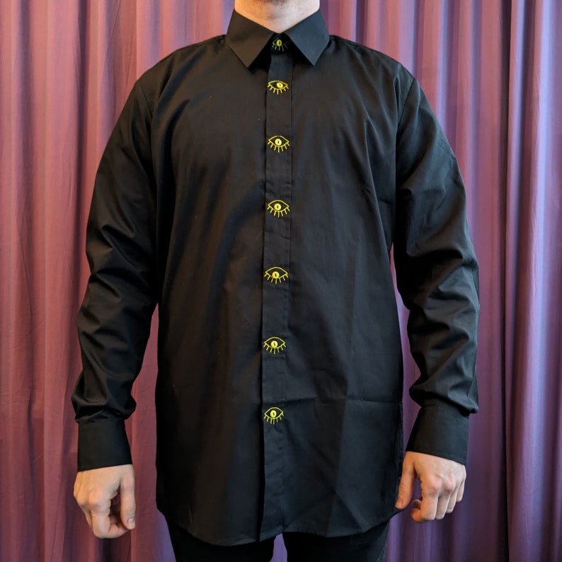 May include: A black long-sleeved button-down shirt with yellow eye buttons.